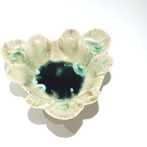 May include: A ceramic bowl with a unique, organic shape. The bowl features a dark blue center and a light beige exterior with green and brown accents. The edges have a scalloped design, adding to its artistic appeal. This decorative bowl is ideal for serving or display.