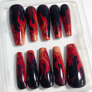 May include: Set of ten long, coffin-shaped false nails with a black and red flame design. The nails are arranged in a clear plastic case.