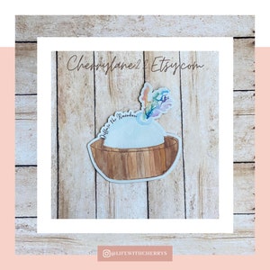 May include: A watercolor sticker featuring a rainbow with the text "Believe the Rainbow" in a wooden bowl. The sticker is on a woodgrain background.