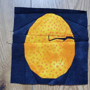 Könnte beinhalten: Ein Quiltblock mit einem gelben und orangen Kreis mit orangen Punkten auf dunkelblauem Hintergrund.