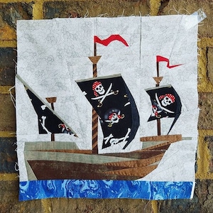 May include: A brown and gray pirate ship with black sails decorated with white skulls and crossbones. The ship has two red flags and is sailing on a blue and white marbled sea.