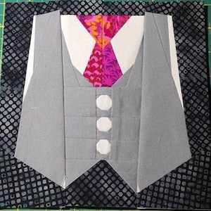 May include: A gray vest with a white shirt and a pink and orange tie. The vest has three white buttons. The background is a black and white patterned fabric.