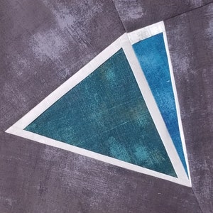 May include: A teal blue triangle with a white border, set against a dark gray background. The triangle is divided into two smaller triangles, one teal blue and one a lighter shade of blue.