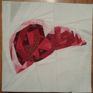 May include: A red and white paper pieced heart with a geometric pattern. The heart is on a white background.