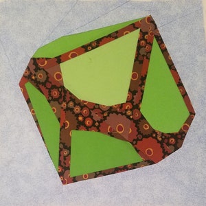 May include: A green geometric shape with a brown and red patterned border. The shape is made of paper and has a three-dimensional appearance.