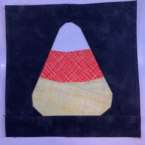 May include: A black fabric square with a white, red, and yellow candy corn applique in the center.