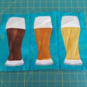 May include: Three glass beer mugs with different colored beer inside. The mugs are white with a gray base and are sitting on a blue background.