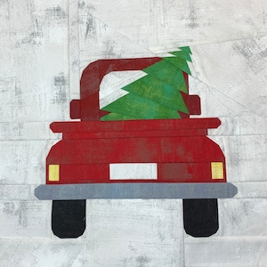 May include: A red pickup truck with a green Christmas tree in the back. The truck has a white number plate and yellow headlights.