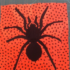 May include: A black spider silhouette on a red fabric background with a white star pattern.