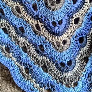 May include: A crocheted blanket with a repeating pattern of blue, gray, and black yarn. The blanket is made with a textured stitch that creates a raised design.