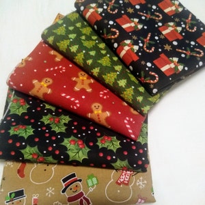 May include: A stack of five Christmas-themed fabric squares. The top square is black with red and white candy canes, presents, and snowflakes. The second square is green with white Christmas trees. The third square is red with white gingerbread men and candy canes. The fourth square is black with green holly leaves and red berries. The bottom square is brown with white snowmen and snowflakes.