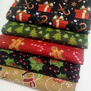 May include: A stack of five different Christmas fabric prints. The prints feature a variety of holiday themes, including presents, candy canes, Christmas trees, gingerbread men, holly, snowmen, and snowflakes. The fabrics are all in a variety of colors, including red, green, black, brown, and white.
