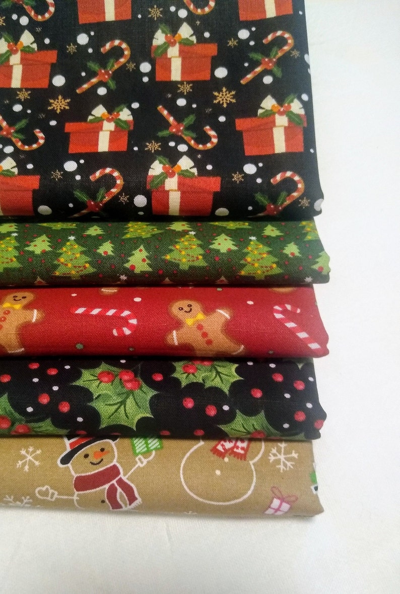 May include: A stack of six different Christmas-themed fabric prints. The top print features red and white presents, candy canes, and snowflakes on a black background. The second print features green Christmas trees on a white background. The third print features red candy canes and gingerbread men on a red background. The fourth print features green holly leaves and red berries on a black background. The fifth print features snowmen and presents on a tan background. The bottom print features a white snowflake pattern on a brown background.