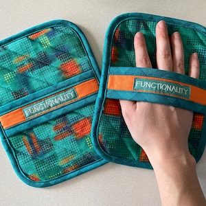 May include: Two teal and orange quilted pot holders with a white "Functionality" label on each. The pot holders have a geometric pattern.