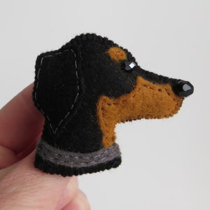 May include: A black and brown felt dachshund dog pin with black bead eyes. The dog is wearing a grey felt collar.
