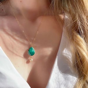 Könnte beinhalten: Eine goldene Kettenkette mit einem tropfenförmigen grünen Edelstein-Anhänger und einer kleinen Perle, die darunter baumelt.