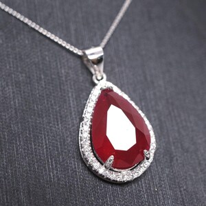 May include: A silver necklace with a teardrop-shaped pendant featuring a large red ruby surrounded by a halo of smaller white diamonds.