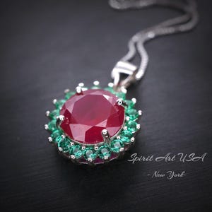 May include: A silver pendant necklace with a large red ruby gemstone surrounded by smaller green gemstones. The pendant is on a silver chain.