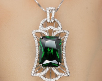 May include: A silver pendant necklace with a large emerald green gemstone set in a detailed, ornate frame. The frame is decorated with smaller clear gemstones.