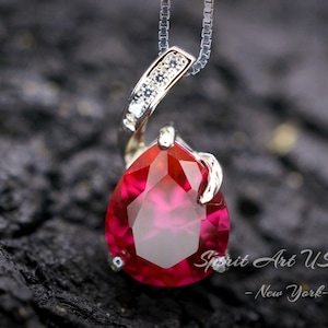 May include: A silver pendant necklace with a teardrop-shaped red gemstone and small clear cubic zirconia stones. The pendant is on a silver chain.