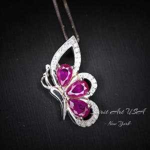 May include: A silver butterfly pendant necklace with three pink ruby stones. The butterfly has clear crystal accents.