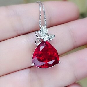 Peut inclure: Un collier en argent avec un pendentif en pierre rouge et un charme papillon. Le charme papillon est serti de pierres de zircone cubique transparentes.