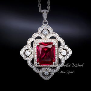 May include: A silver pendant necklace with a large, red, rectangular gemstone surrounded by smaller, clear gemstones. The pendant is in a decorative, ornate design.