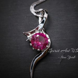 May include: A silver necklace with a pink gemstone pendant. The pendant is shaped like a swirl with a large, round, faceted gemstone in the center.