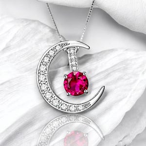 May include: A silver crescent moon pendant necklace with a pink gemstone in the centre. The moon is adorned with small clear stones.