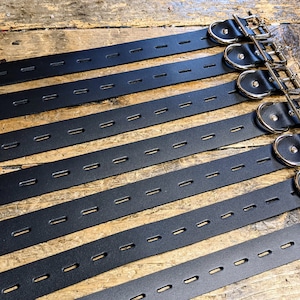 May include: Eight black leather straps with silver metal buckles and D-rings. The straps have multiple rows of evenly spaced holes.