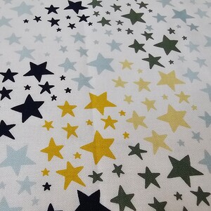 May include: White fabric with a repeating pattern of stars in various sizes and colors. The stars are navy blue, yellow, olive green, and light blue. The stars are scattered across the fabric.