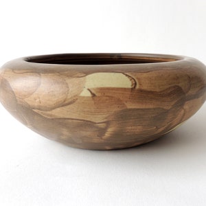 May include: A large, brown ceramic bowl with a wide, shallow shape and a mottled, marbled glaze. The glaze features shades of brown, tan, and cream.