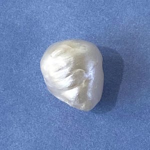 May include: A pearlescent, off-white, irregularly shaped object, possibly a pearl or a decorative element, rests against a textured blue background. The object has a smooth, reflective surface with subtle highlights and shadows.