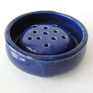 May include: A deep blue ceramic flower frog with a round base and a circular top with multiple holes for arranging flowers.