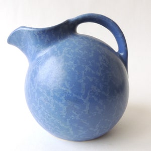 May include: A blue ceramic pitcher with a mottled glaze. The pitcher has a round body and a handle.