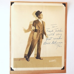 May include: A black and white photograph of a man in a suit and hat. He is standing with his right hand raised. The photo is signed "To Frank Tricher with very best wishes Biel Robinson 1923".
