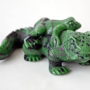 May include: A green jade carving of a frog sitting on top of a larger lizard. Both animals have black spots.