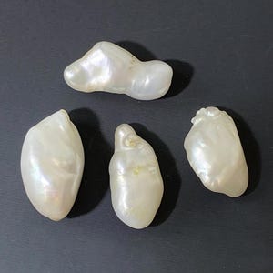 May include: Four irregularly shaped, lustrous white pearls with iridescent surfaces are displayed against a dark background. The pearls vary in size and shape, showcasing natural formations. These could be used for jewelry making.