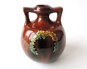 May include: A small, brown ceramic vase with two handles and a floral design. The vase has a glossy finish and is decorated with a green, yellow, and orange floral motif.
