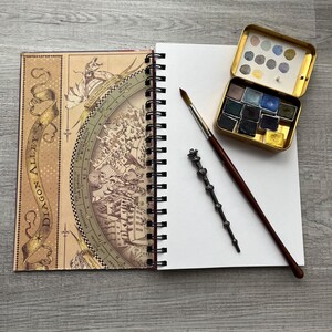 May include: A spiral bound notebook with a map of Diagon Alley on the cover, a paintbrush, a wand, and a watercolor paint set in a tin box.