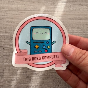 Puede incluir: Una pegatina con un personaje de consola de videojuegos azul sonriente de estilo retro con brazos. El personaje está dentro de un círculo azul claro con un borde rosa. Una pancarta rosa debajo dice "THIS DOES COMPUTE!"