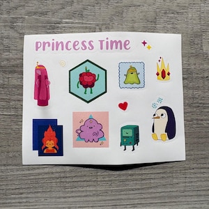 以下が含まれることがあります： アニメシリーズAdventure Timeのキャラクターとアイコンが描かれたステッカーシート。ステッカーには、プリンセス・バブルガム、ラズベリーのキャラクター、王冠、ペンギン、そして「princess time」の文字が含まれています。