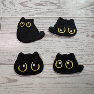 May include: Four black cat-shaped embroidered patches. Each patch features a solid black silhouette with large, round, yellow-outlined eyes and white pupils. The cats are depicted in various poses, including sitting and lying down, with distinct ear shapes and tails.