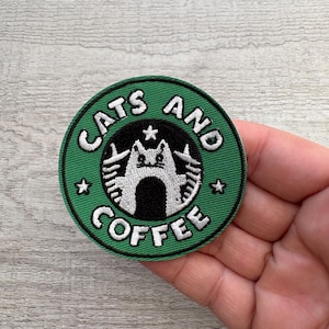 Op de afbeelding: Een ronde, groene patch met de witte tekst "CATS AND COFFEE" in een boog. In het midden een wit katten silhouet op een zwarte achtergrond. De patch heeft een zwarte rand en ster accenten.