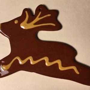 May include: A brown ceramic reindeer ornament with yellow painted details. The reindeer is in a leaping pose with a wavy line painted on its body.