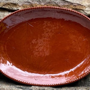 May include: A large, oval, terracotta serving platter with a glossy finish. The platter has a raised rim and a subtle leaf design.