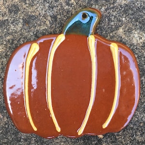 May include: A ceramic pumpkin decoration with a glossy, reddish-brown body and a teal-colored stem. The pumpkin has vertical yellow stripes. This fall-themed decor is perfect for seasonal displays.
