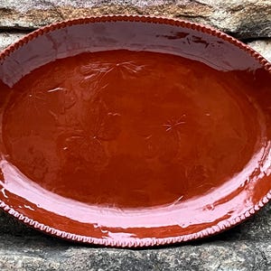 May include: A large, oval, terracotta serving platter with a glossy finish. The platter has a decorative, embossed design of stylised flowers.