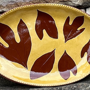 May include: An oval ceramic serving platter with a yellow glaze and a brown leaf design. The leaves are stylized and have a unique shape.