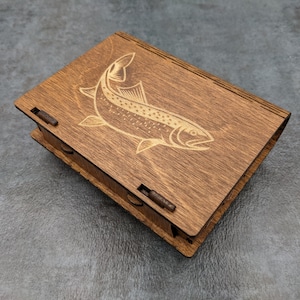 May include: A wooden box with a hinged lid, featuring a laser-engraved design of a trout fish. The box has a dark brown stain and metal hinges.